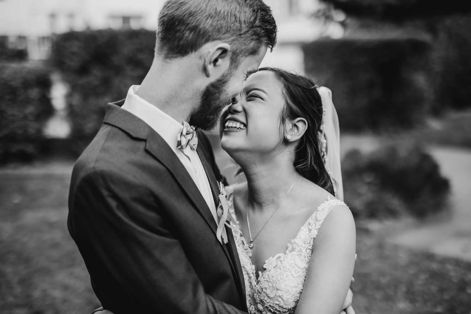 Black and white photo of a couple sharing a joyful moment in their wedding attire.