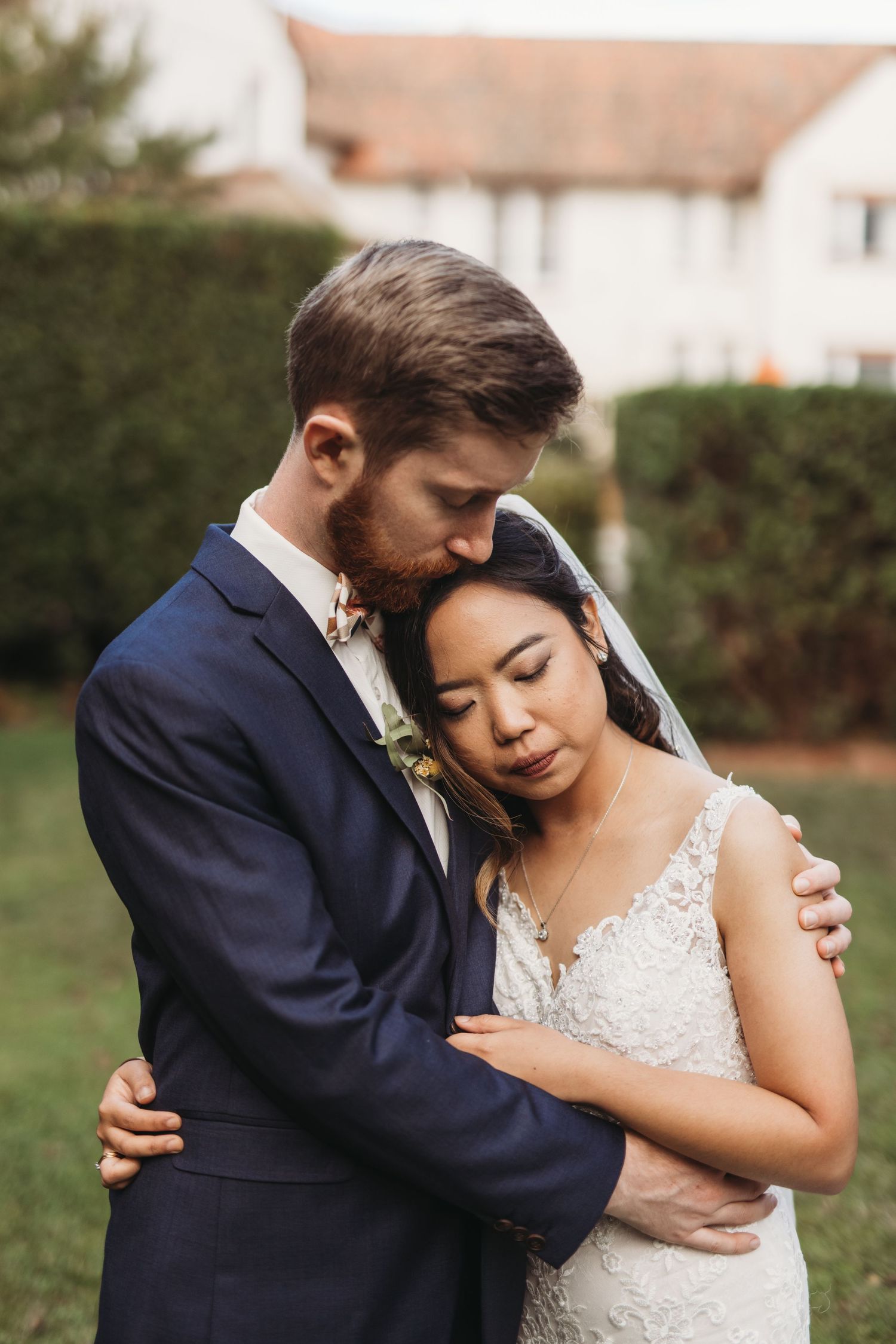 A tender embrace between newlyweds in formal attire against a garden backdrop.