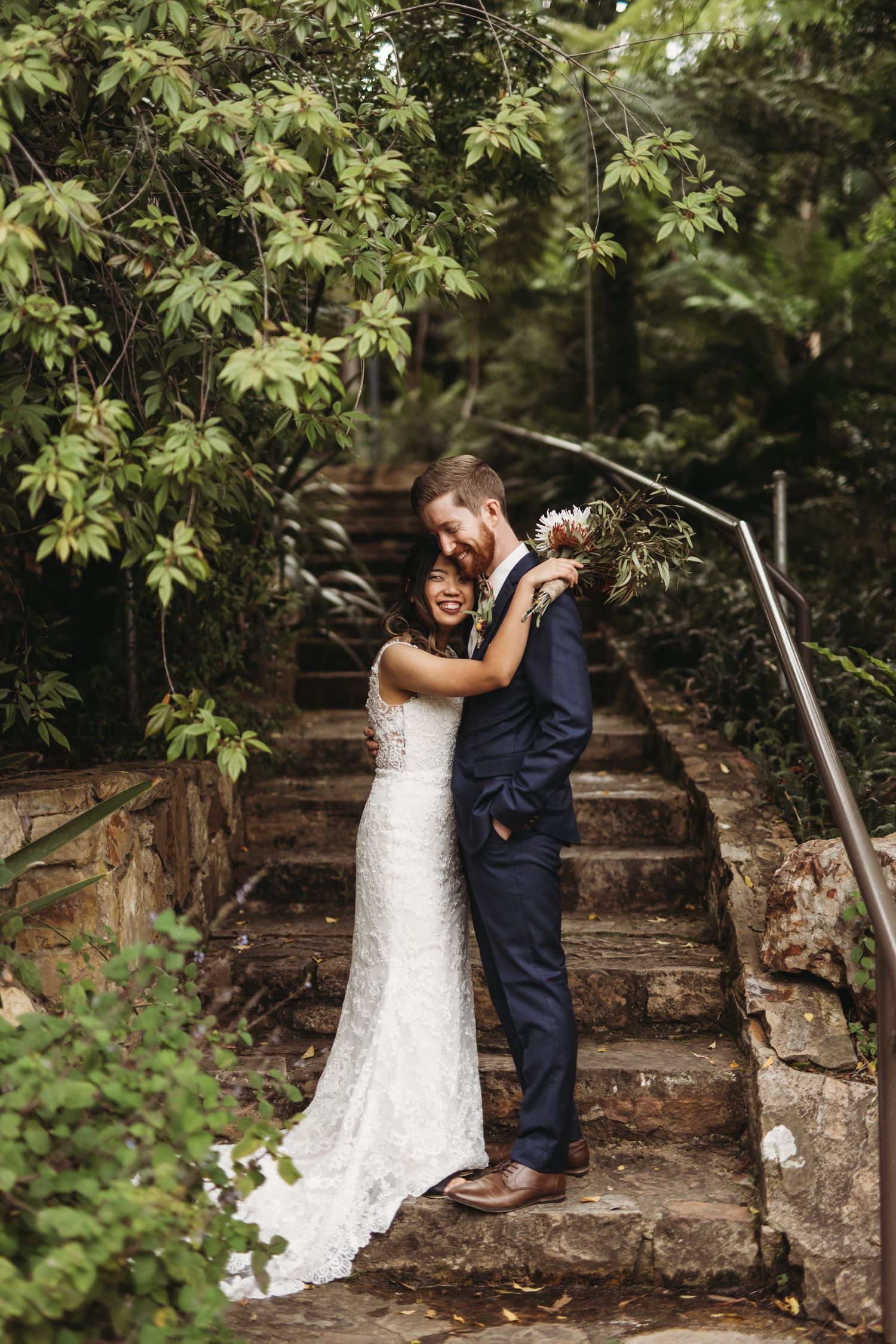 A romantic moment between newlyweds on stone garden steps surrounded by greenery.