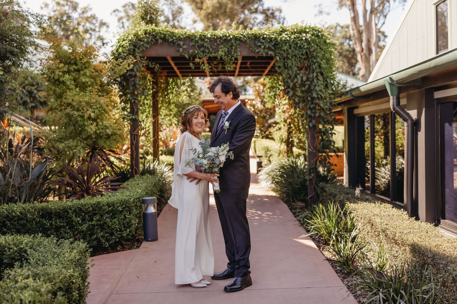 A romantic moment under a vine-covered archway in a garden setting.