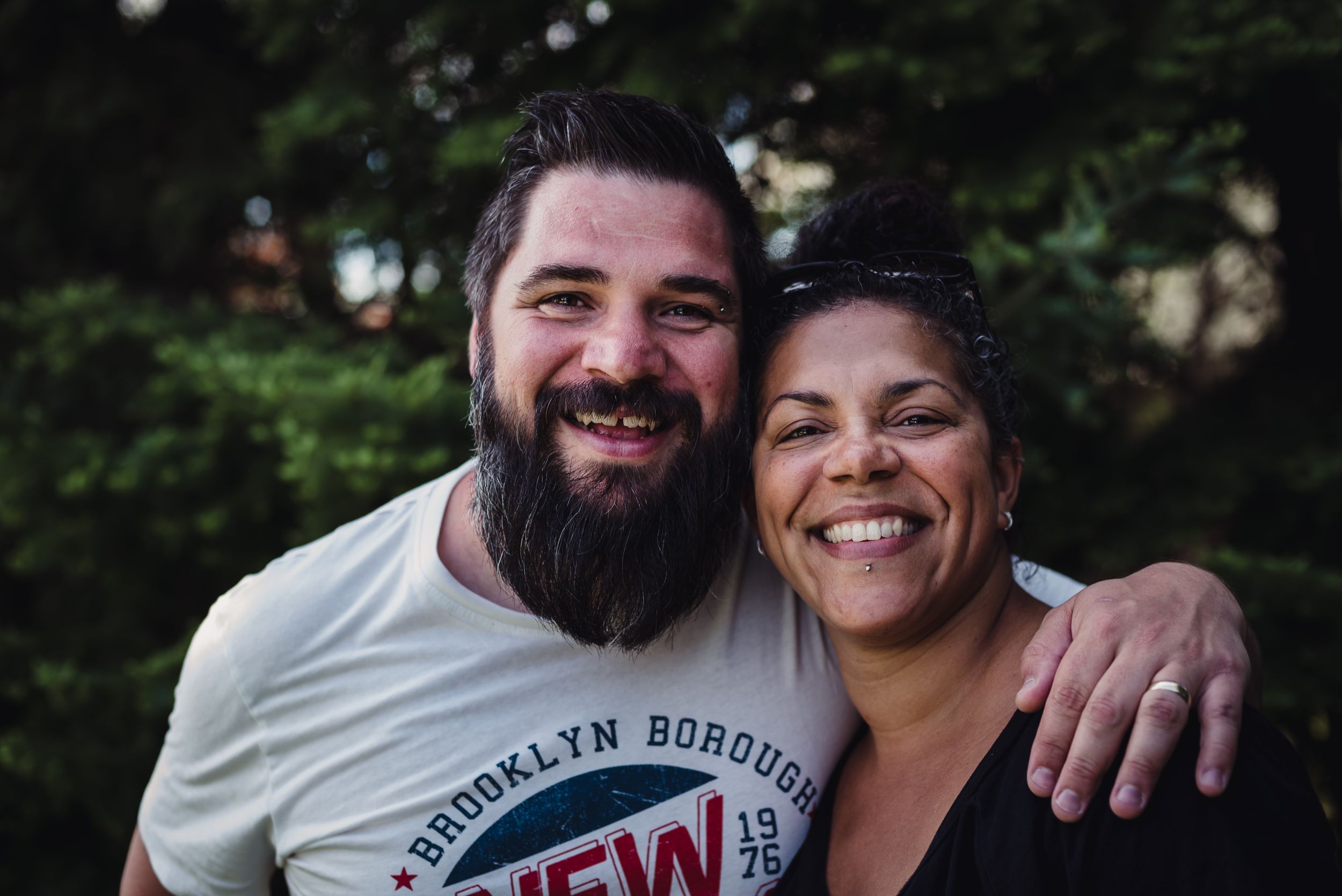 Colour image of a man with his arm around his wife's shoulder as both smile at the camera.