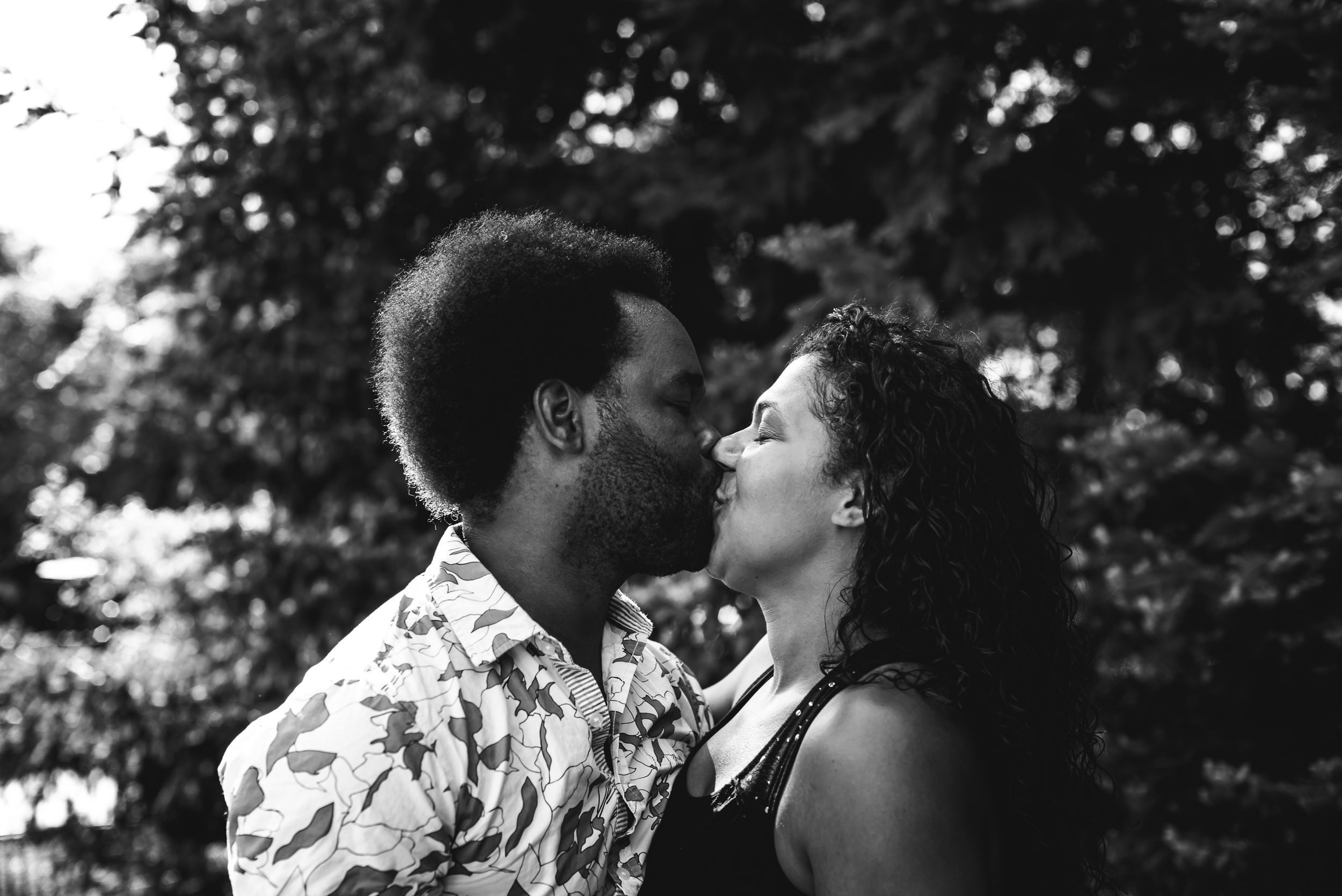 BW image of a couple kissing with pines in the background.