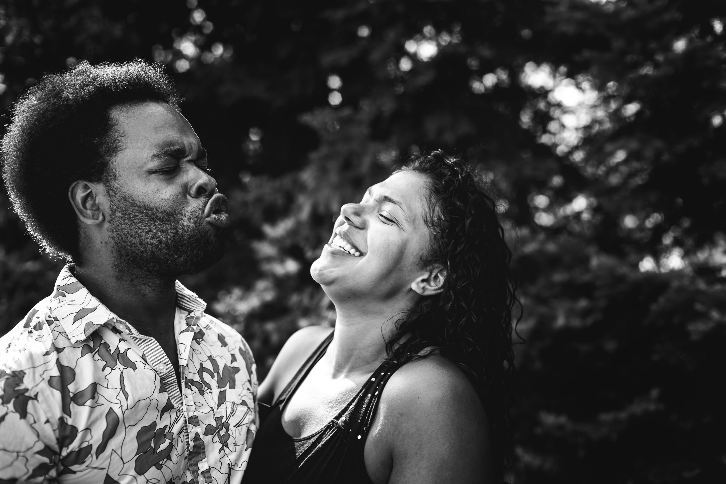 BW image of a black man making a funny duck face as his wife looks at him and laughs.