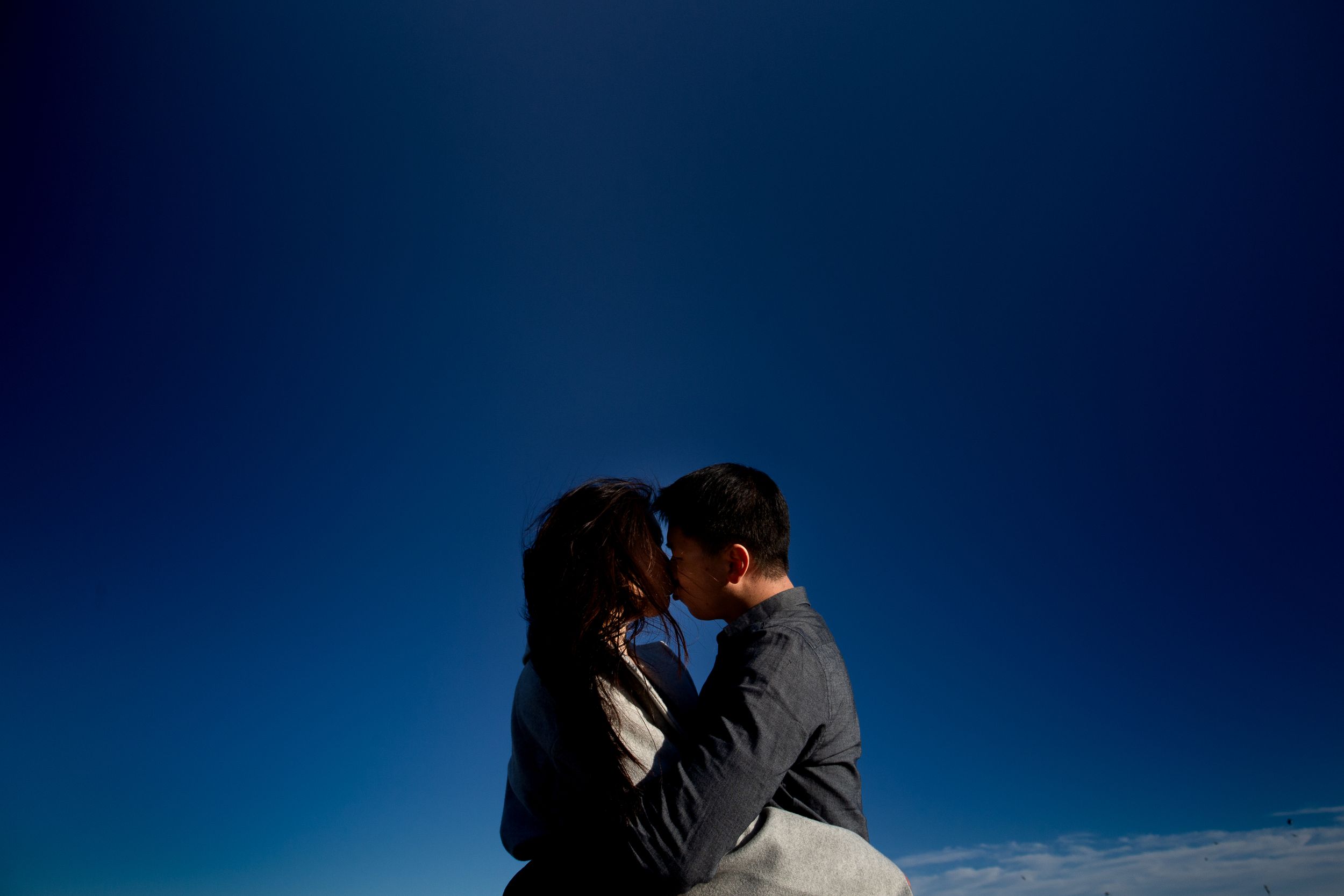 An intimate silhouette moment against a deep blue sky at the seaside.