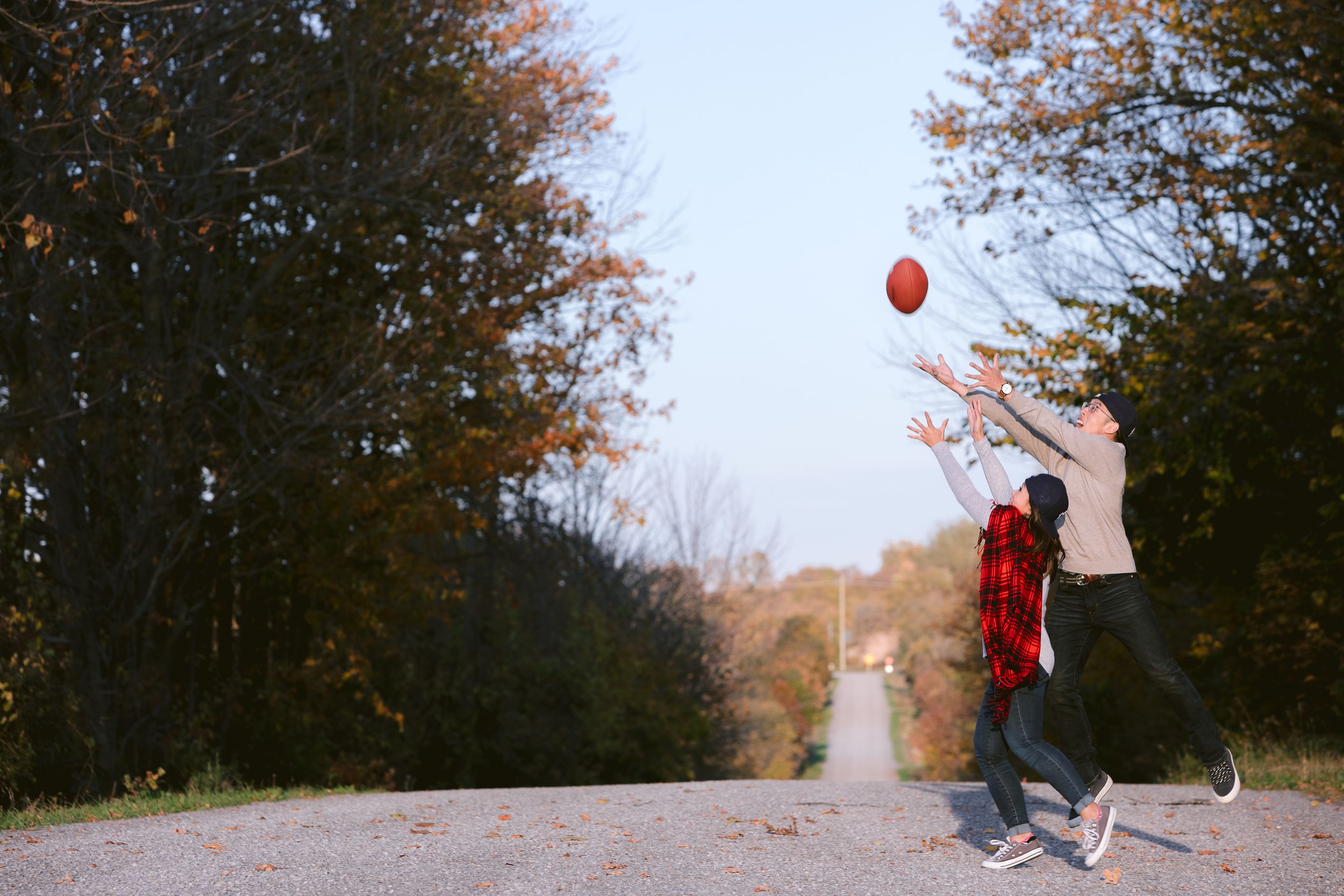 A person in red jumps while holding a balloon on a rural path during autumn.