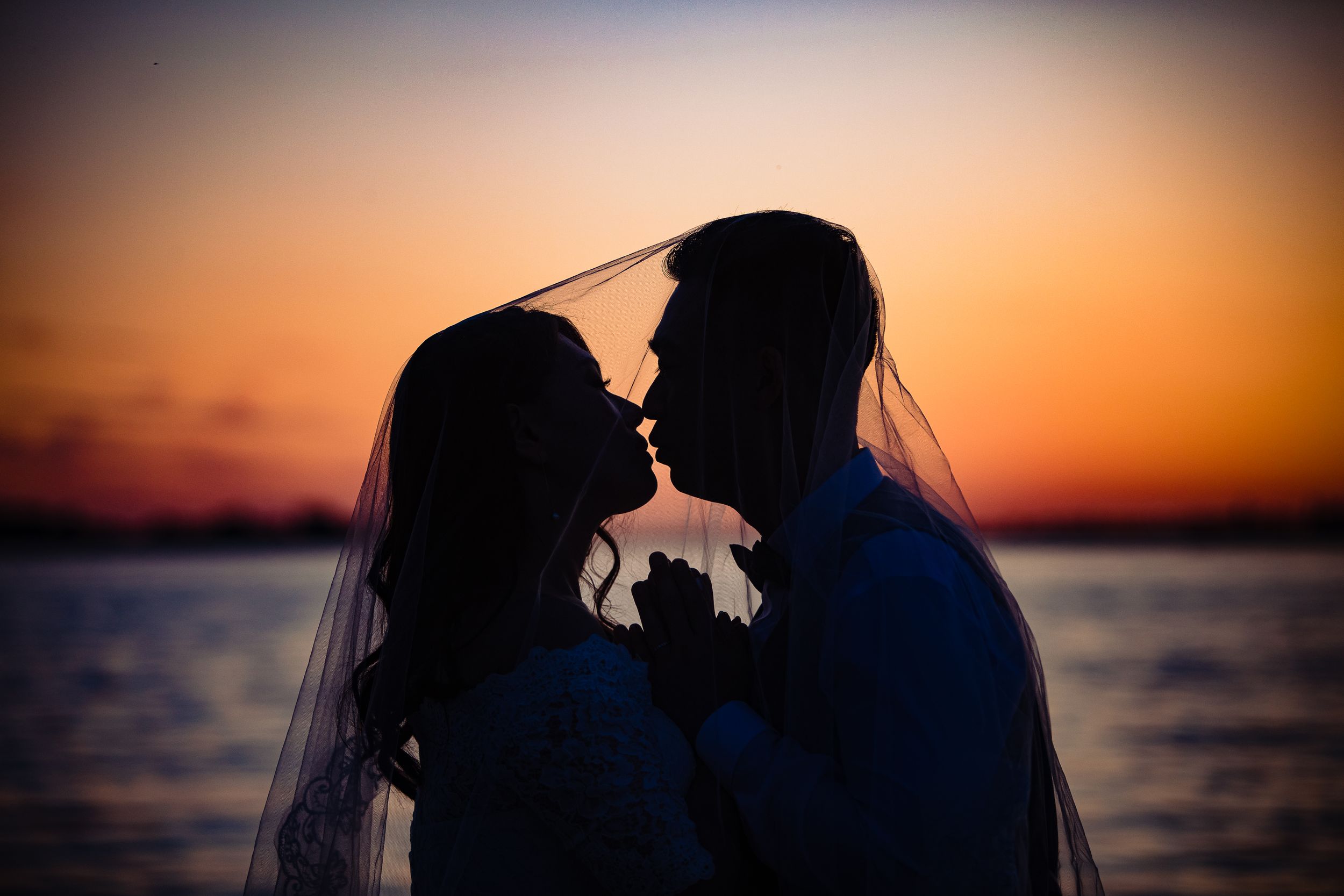 A romantic silhouette against a vibrant orange sunset over water.