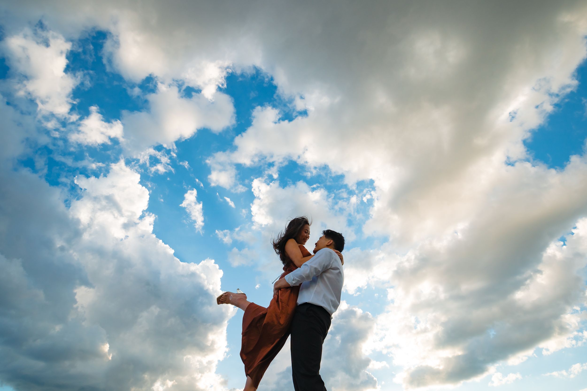 A joyful embrace captured against a dramatic cloudy sky during golden hour.