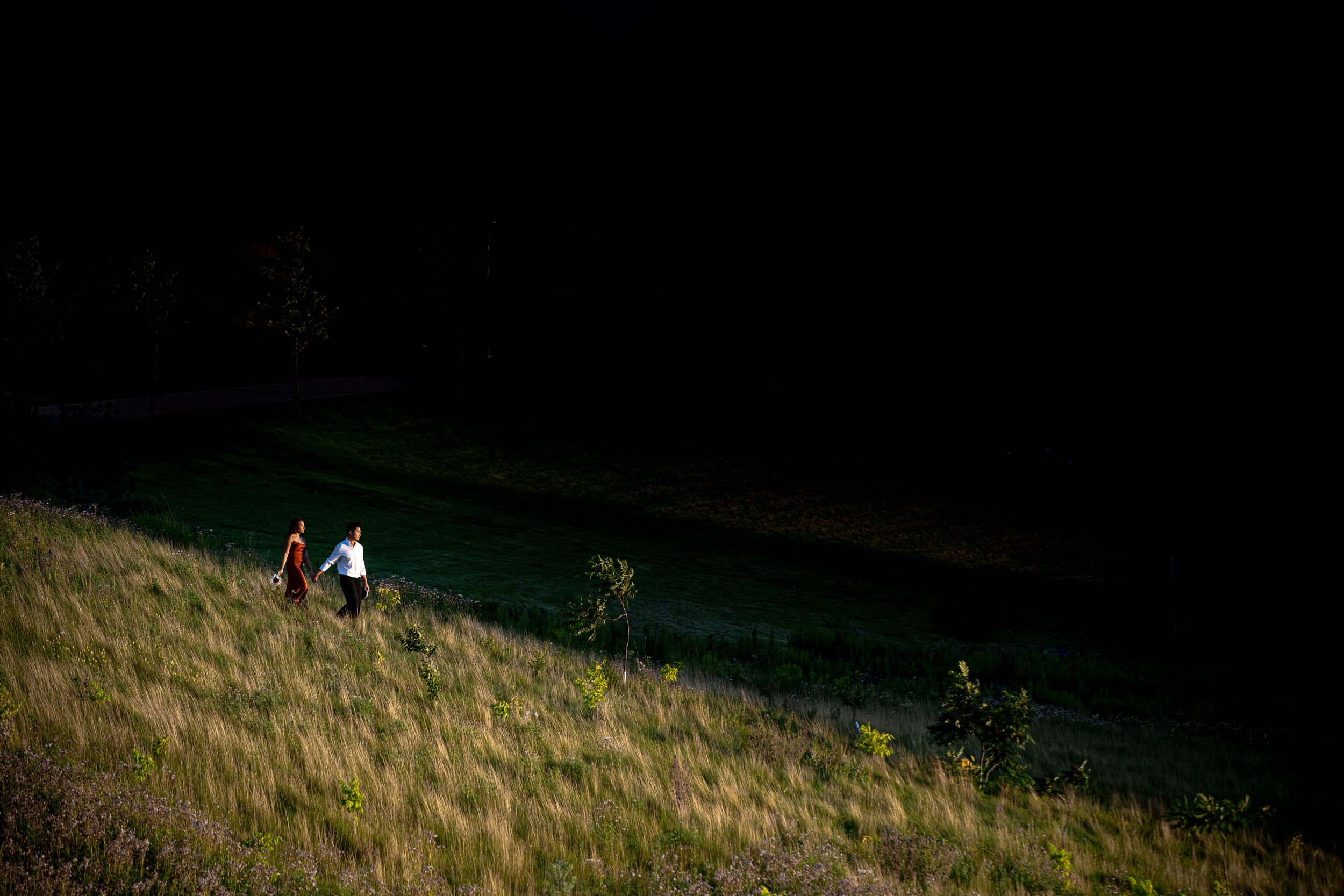A distant couple walks together on a sunlit grassy hillside during late afternoon.