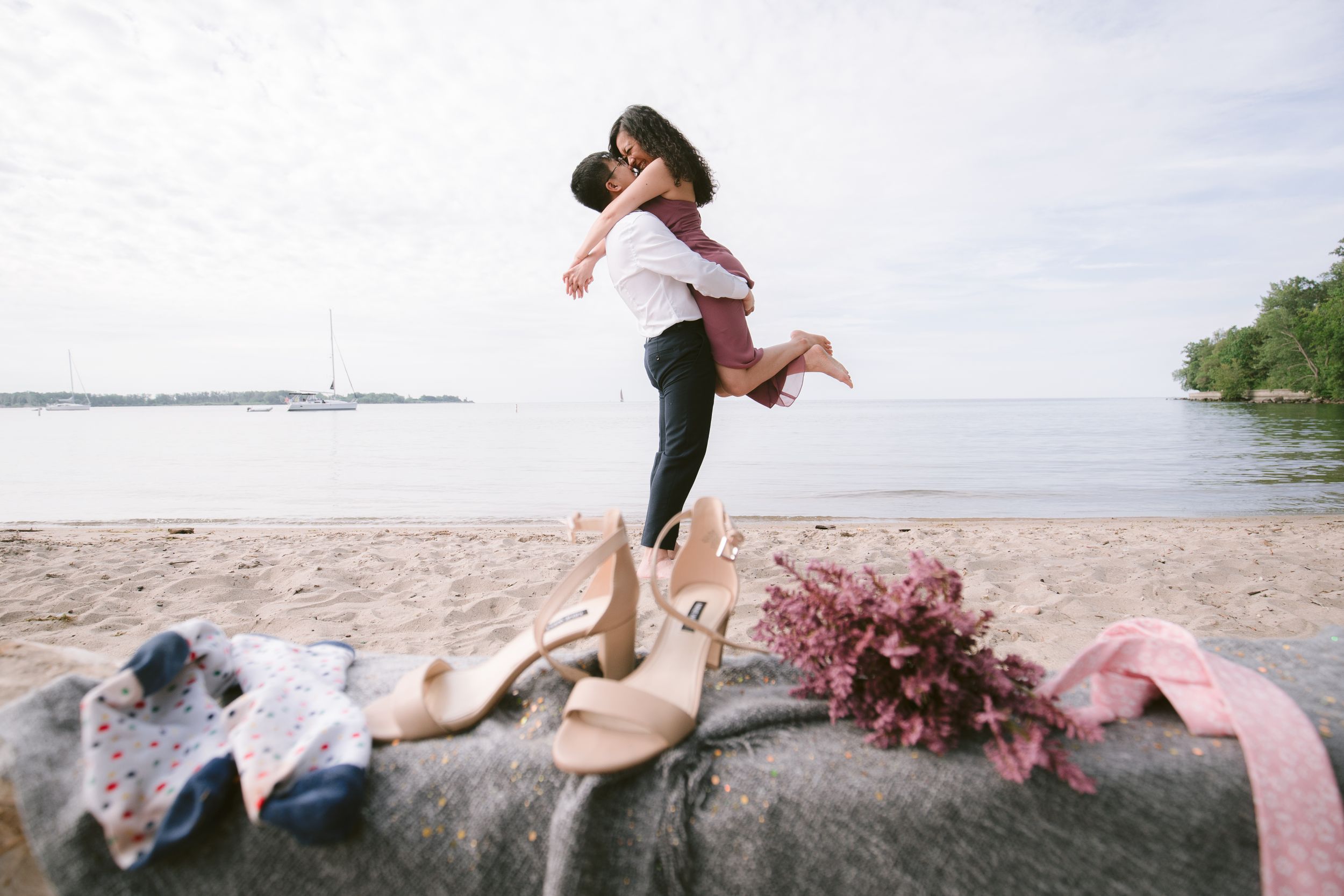 A couple celebrating their engagement with a playful lift by the ocean.