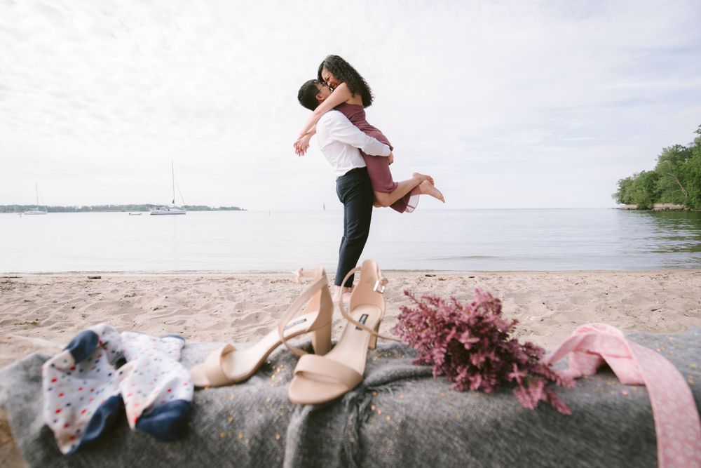 A couple celebrating their engagement with a playful lift by the ocean.