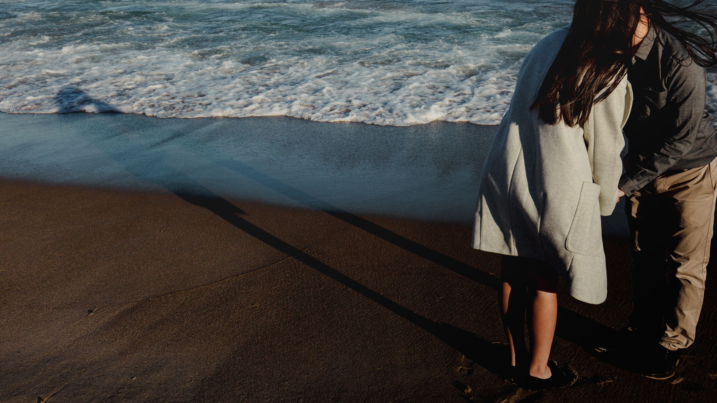 Romantic couple standing on dark sandy beach with ocean waves rolling in.