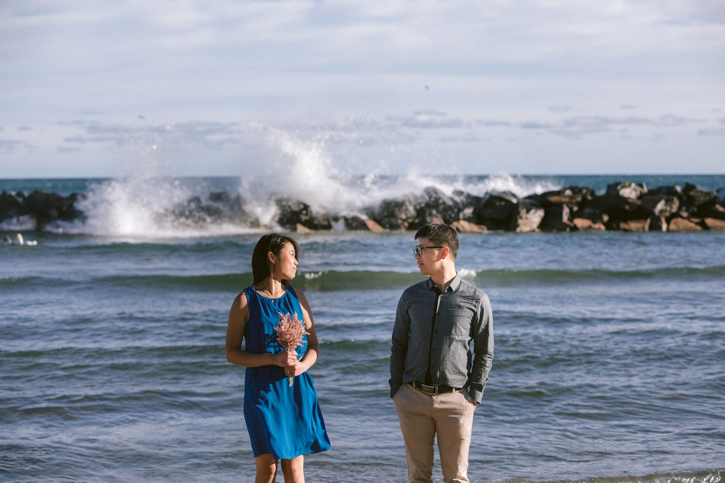 A couple enjoys a scenic moment by crashing ocean waves on a rocky coastline.