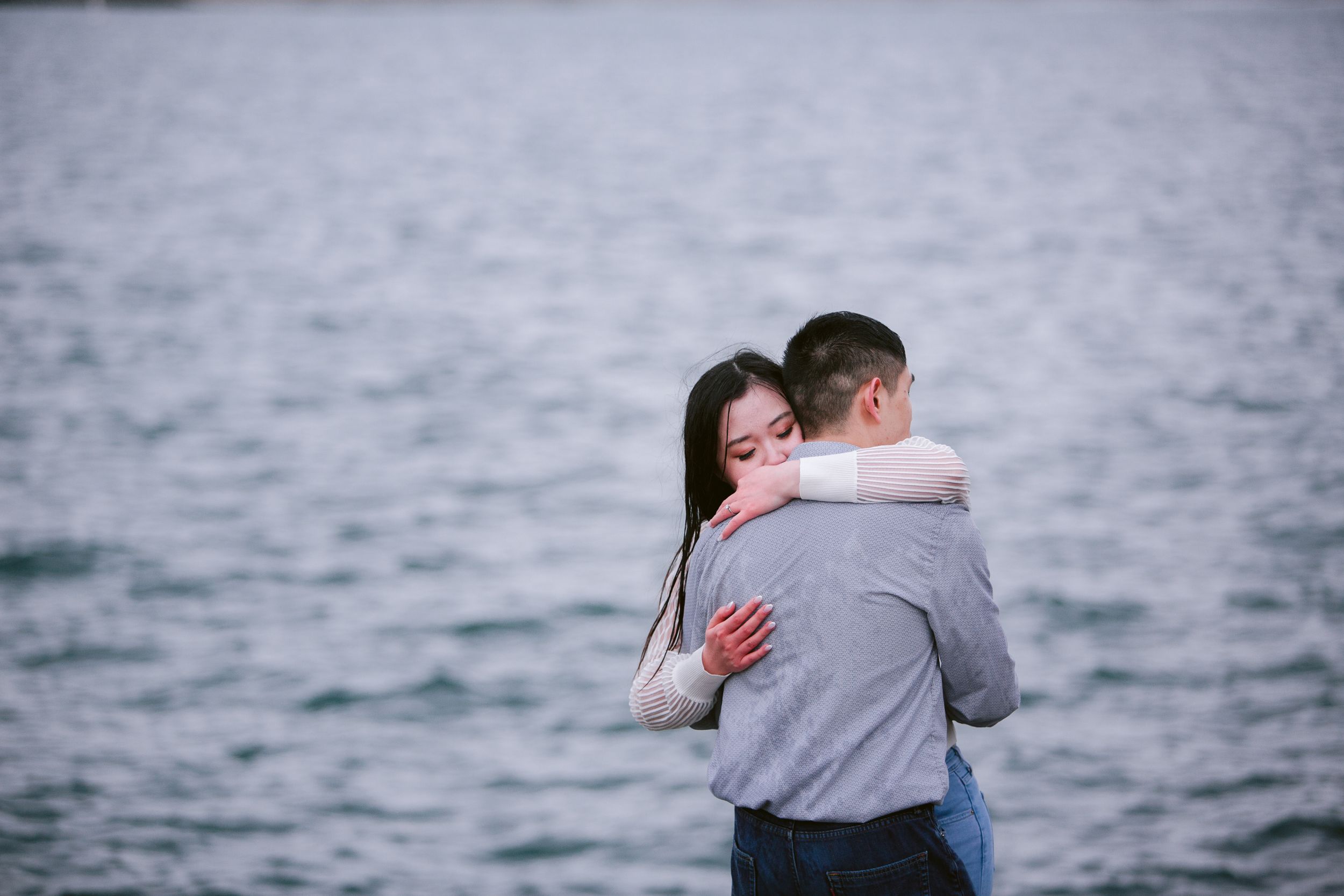 A couple embraces by the ocean during an overcast day.