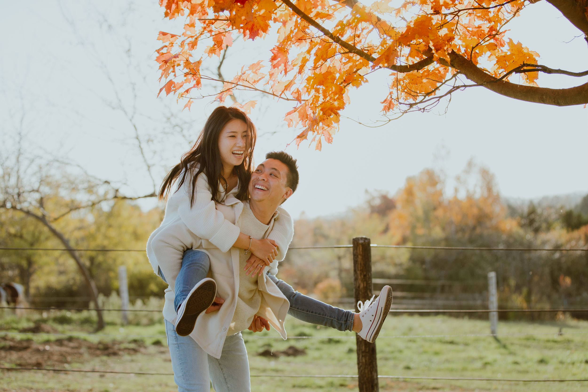 A playful autumn scene with a piggyback ride under orange fall foliage.