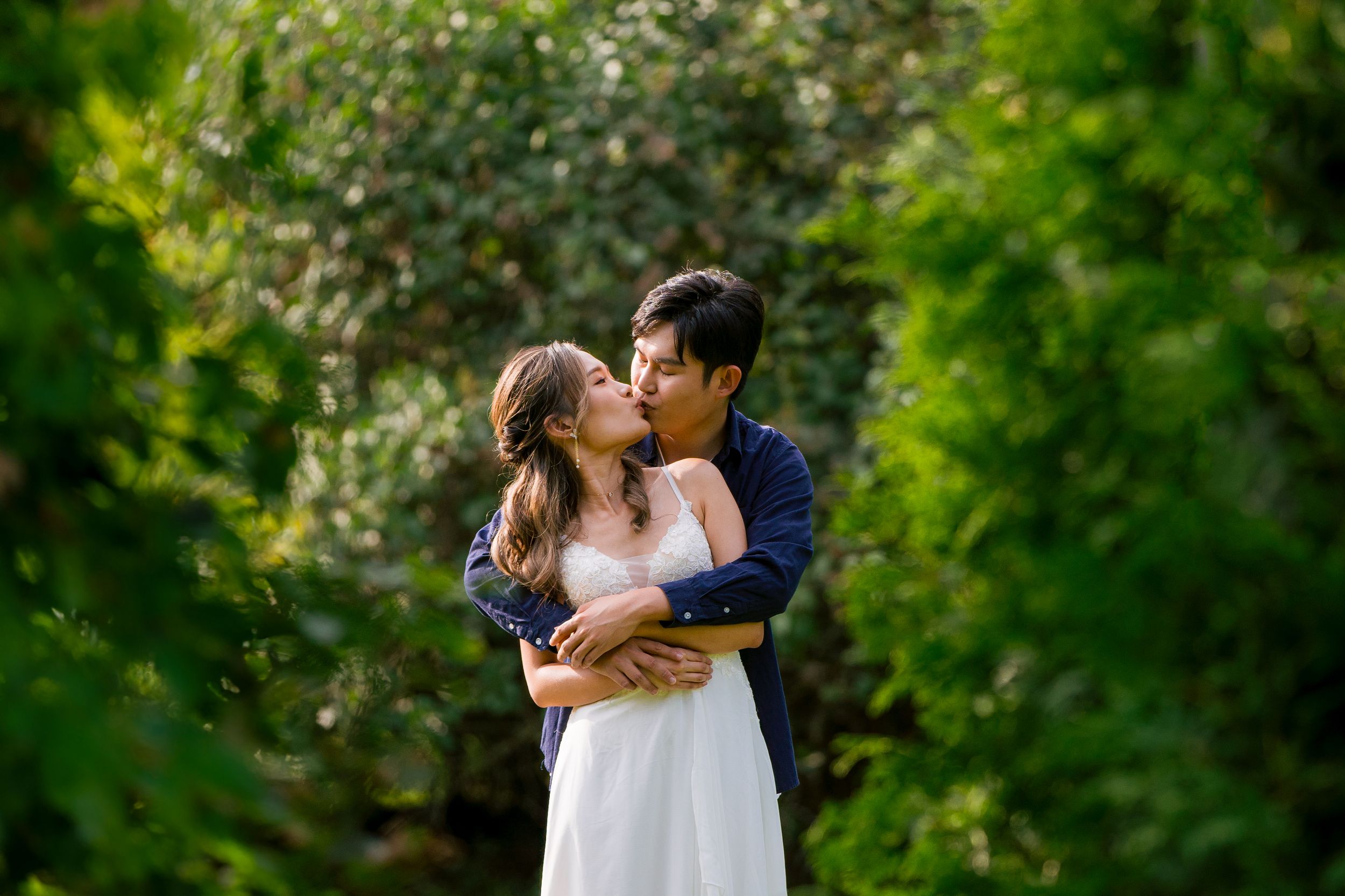 Romantic embrace between couple surrounded by lush green foliage.