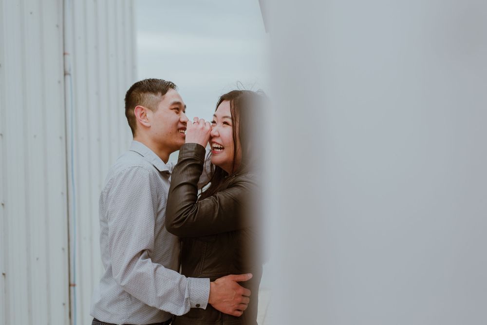 A couple shares a tender moment as they laugh together against a white wall.