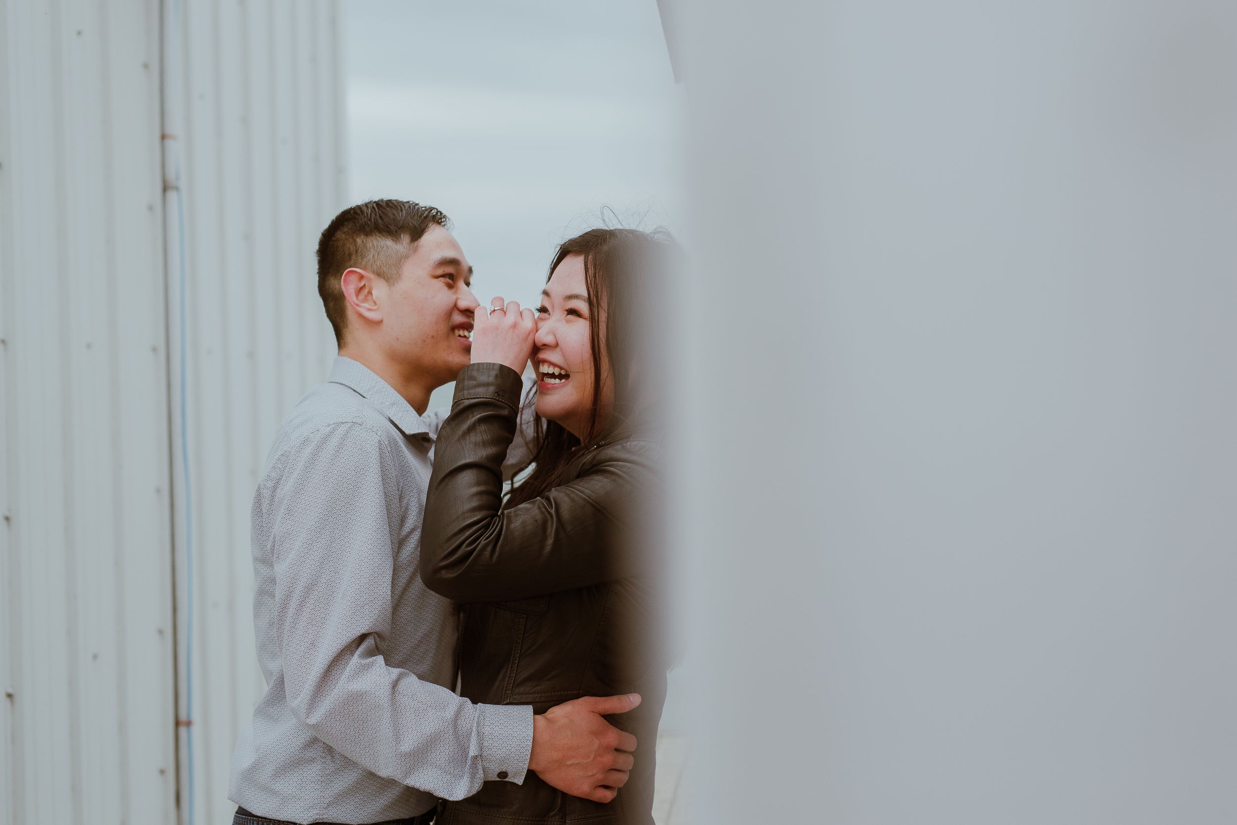 A couple shares a tender moment as they laugh together against a white wall.