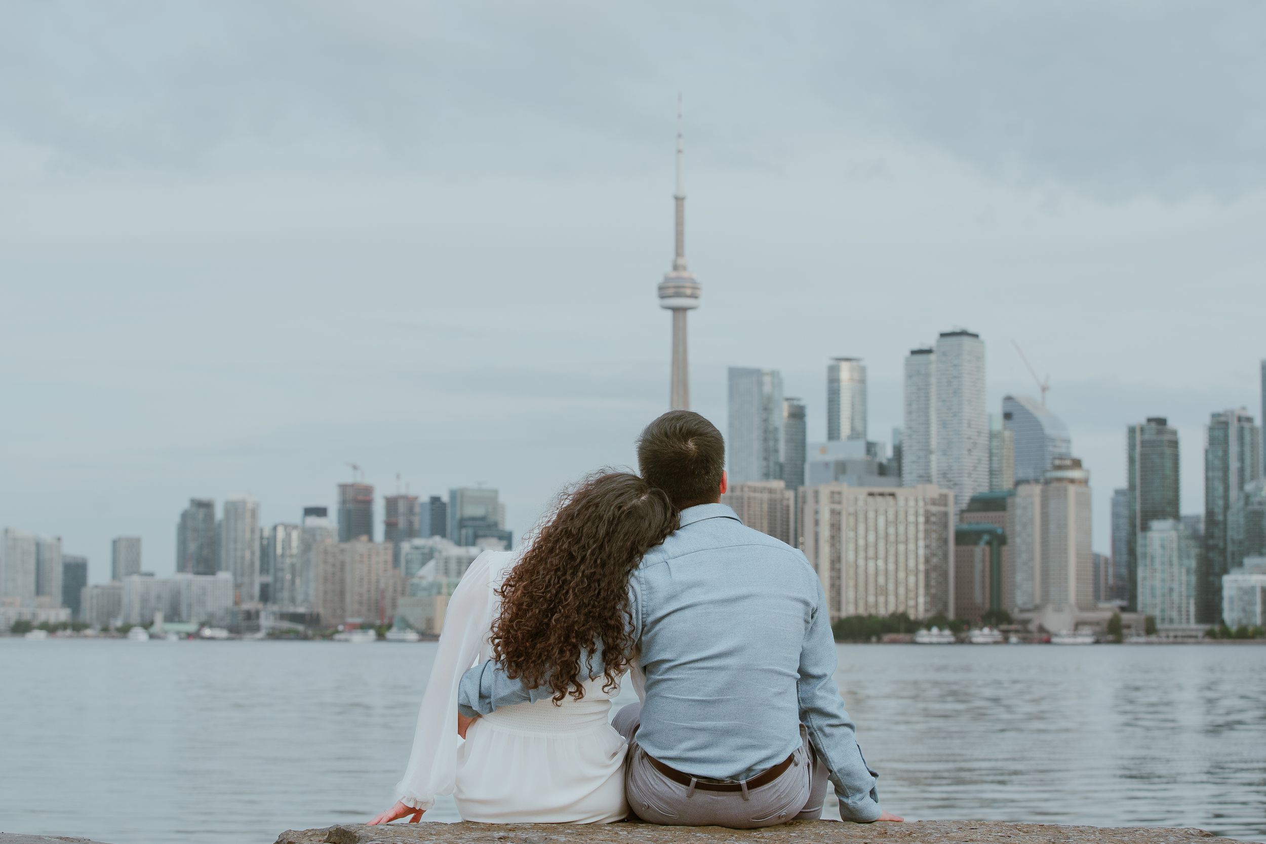 A couple sits by the waterfront overlooking Toronto's iconic skyline.