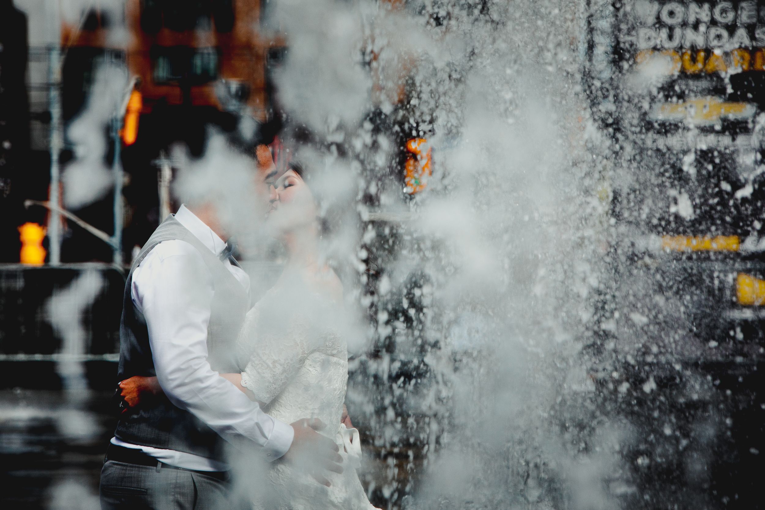 Couple embraces in a dramatic urban setting with water splashing around them.