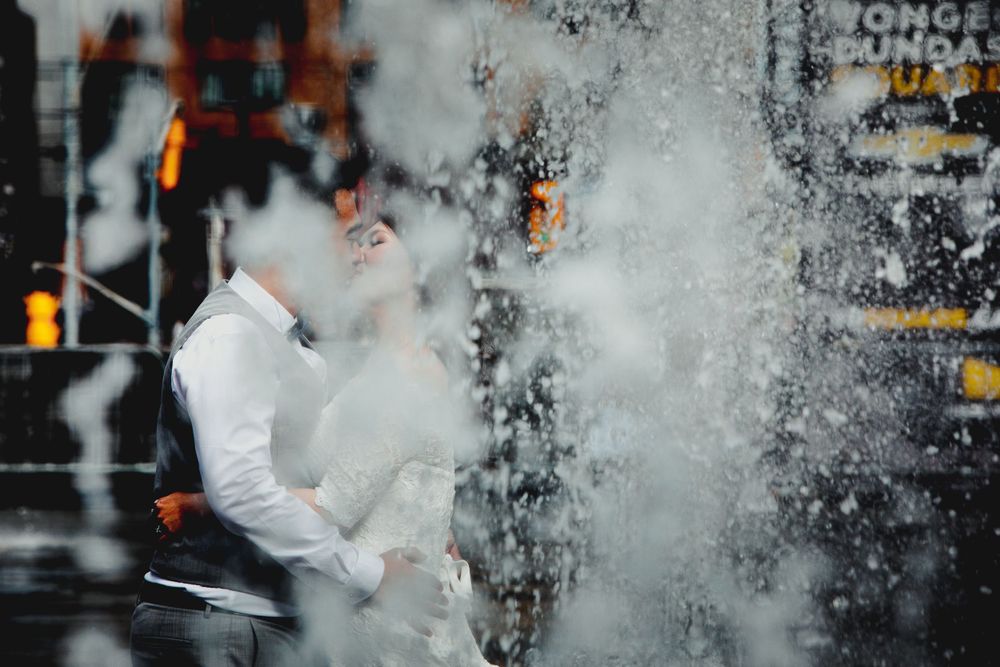 Couple embraces in a dramatic urban setting with water splashing around them.