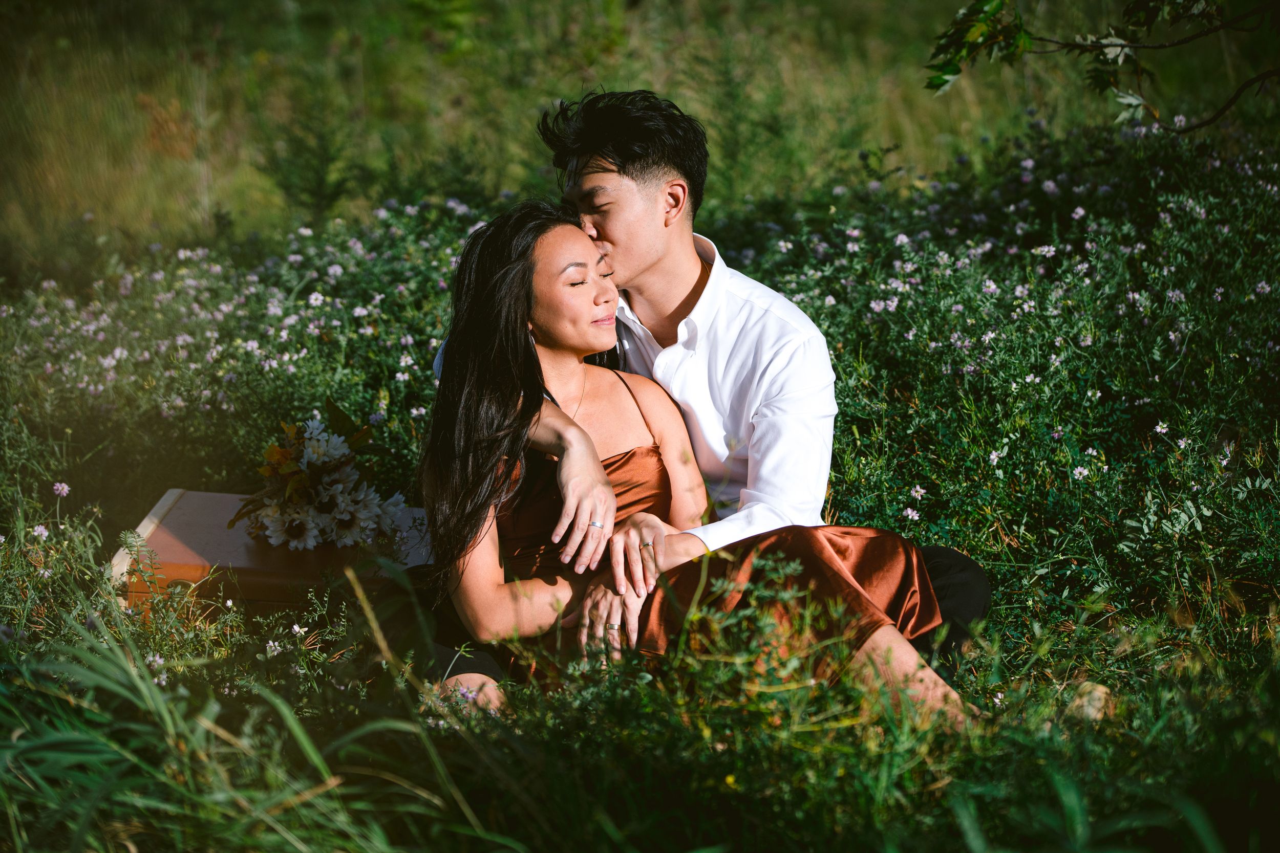 A romantic couple shares an intimate moment while sitting in a wildflower meadow on a sunny afternoon.