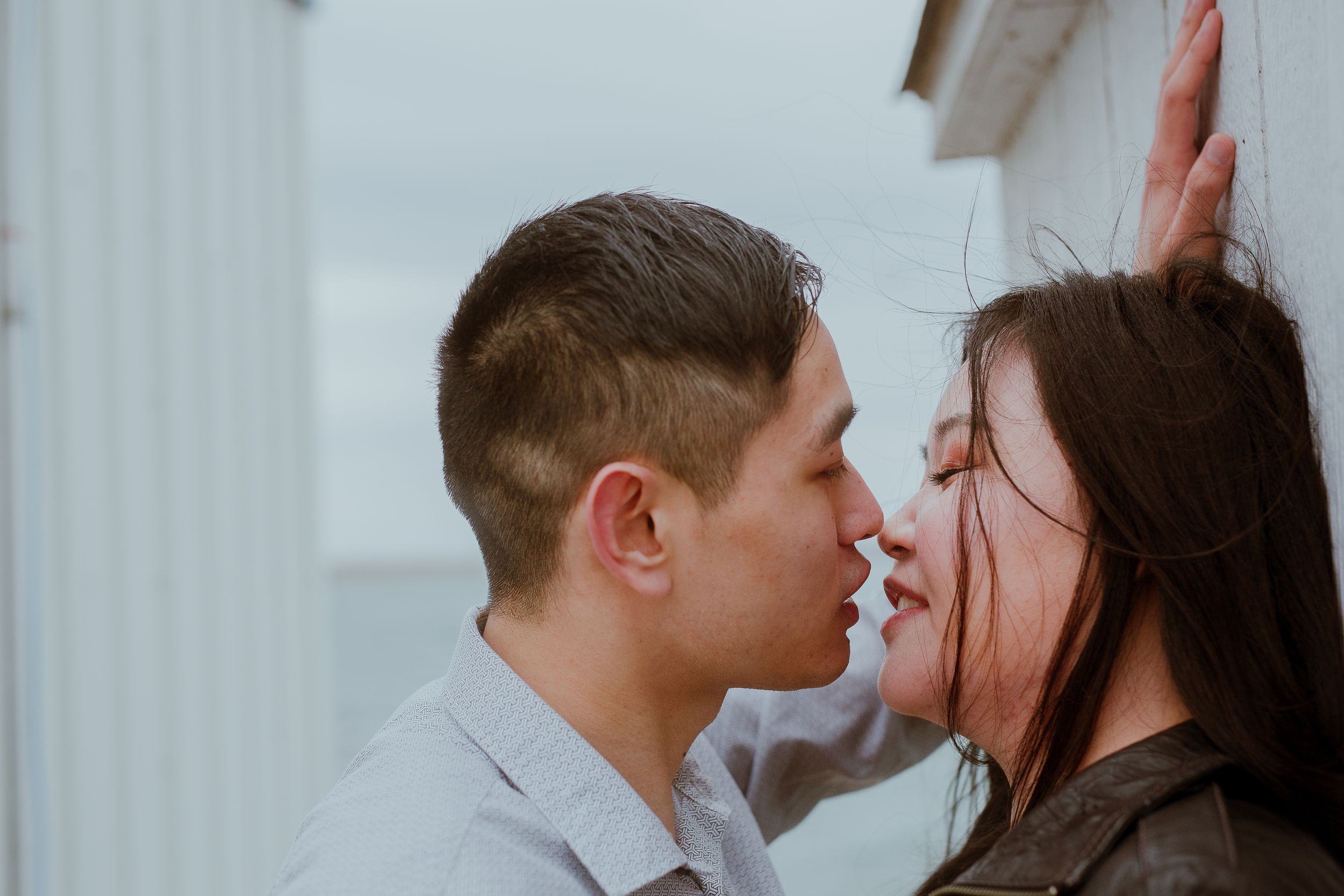 A romantic close-up of a couple sharing an intimate moment against a white wall.