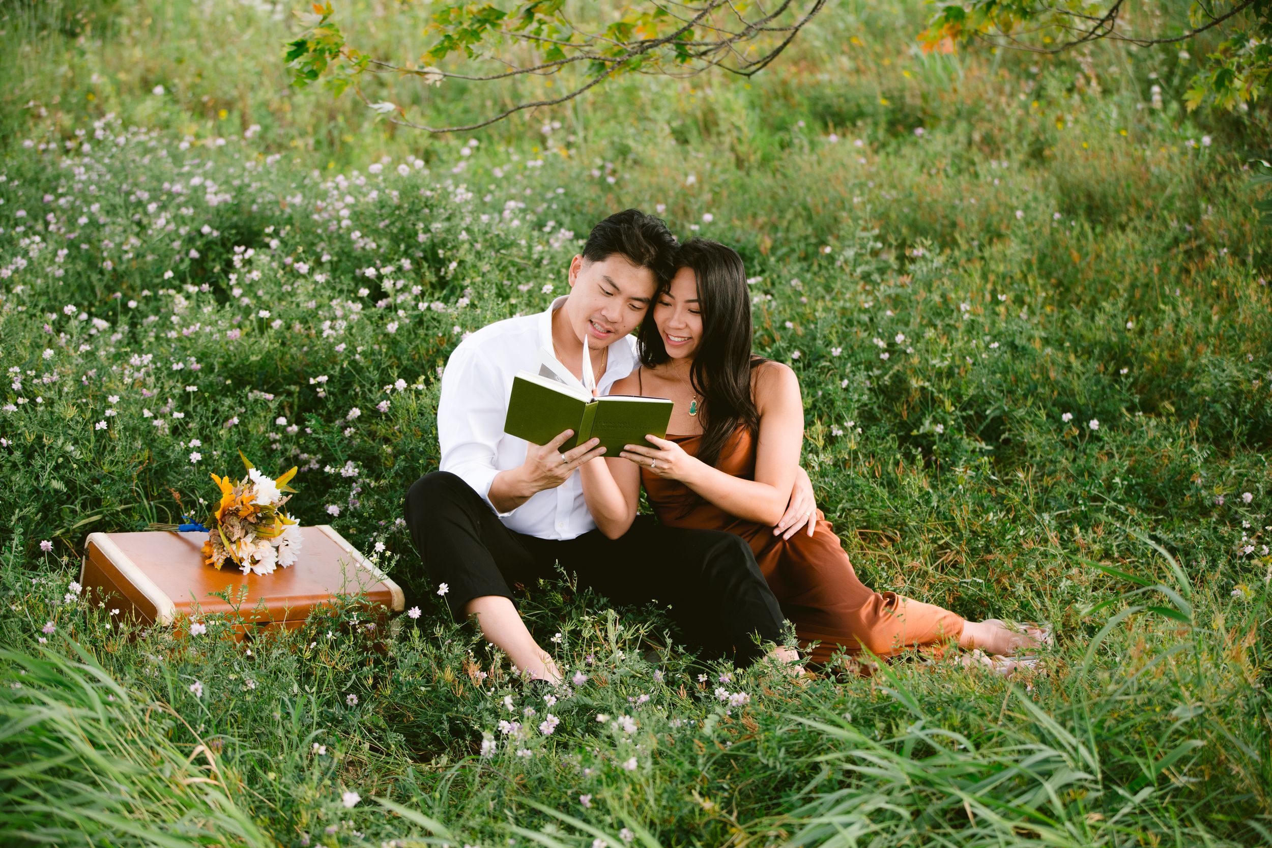 Couple reading together while relaxing in a wildflower meadow with a picnic setup.