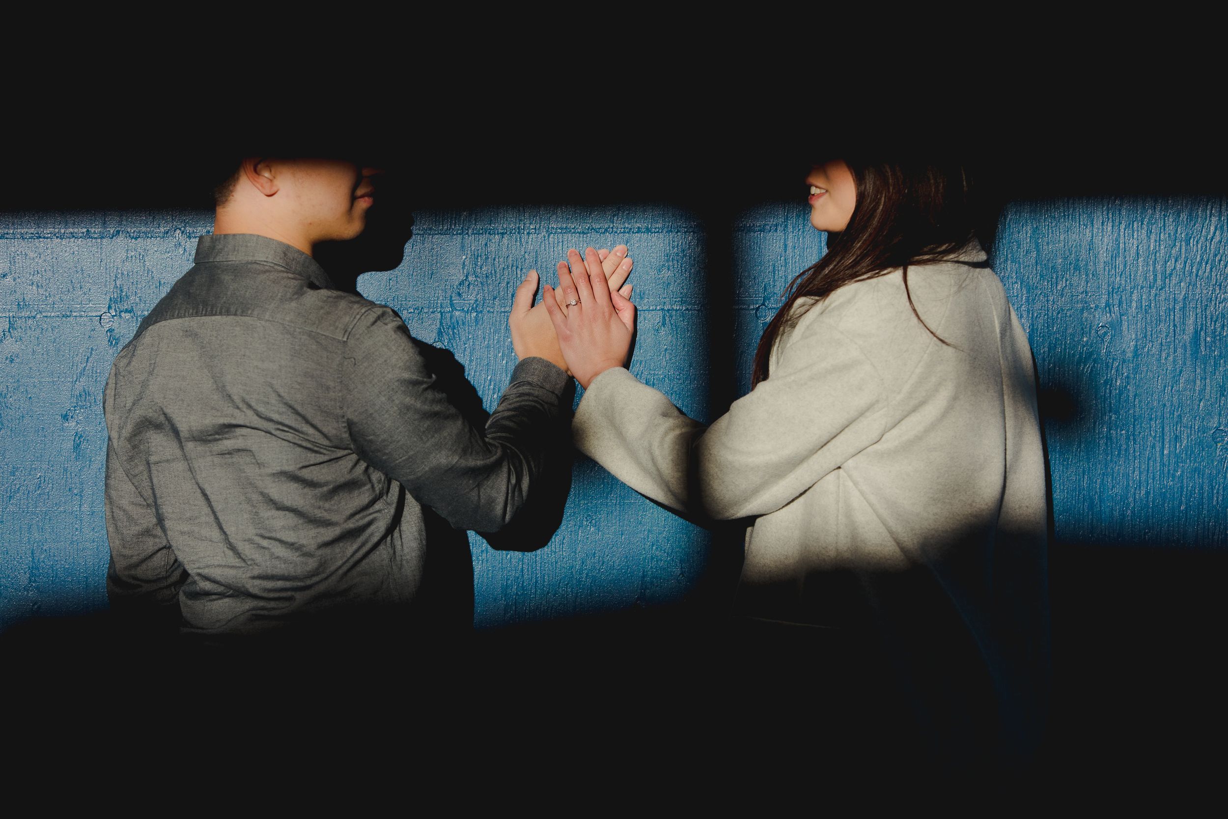 Two people sitting in shadows reaching out to hold hands.