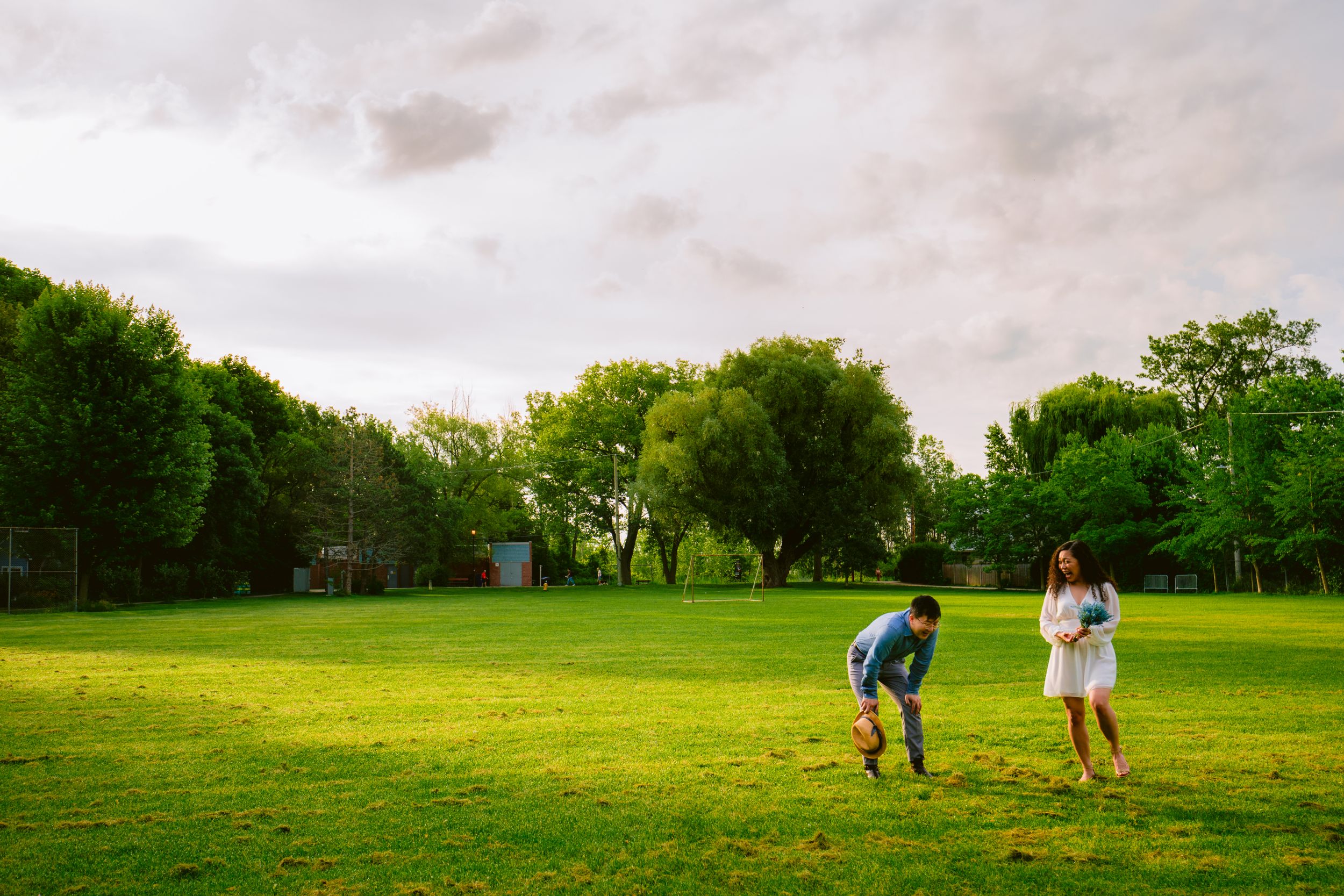A couple runs playfully through a green field during sunset.