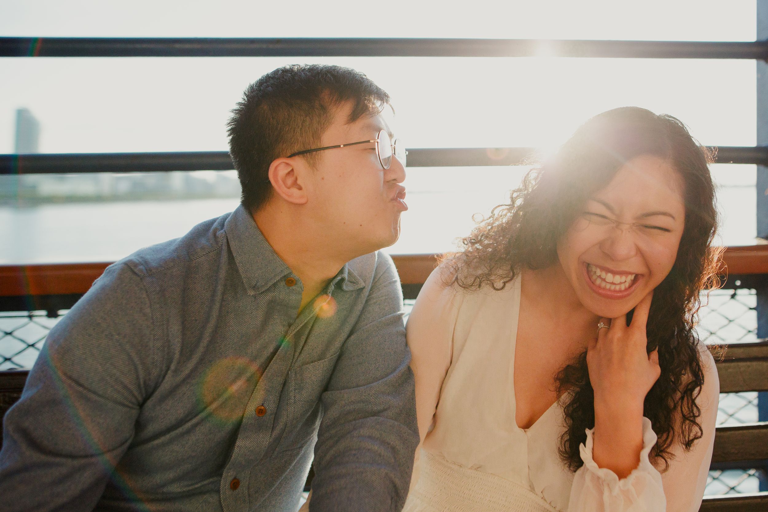 A couple laughs together during a sunlit engagement photoshoot.