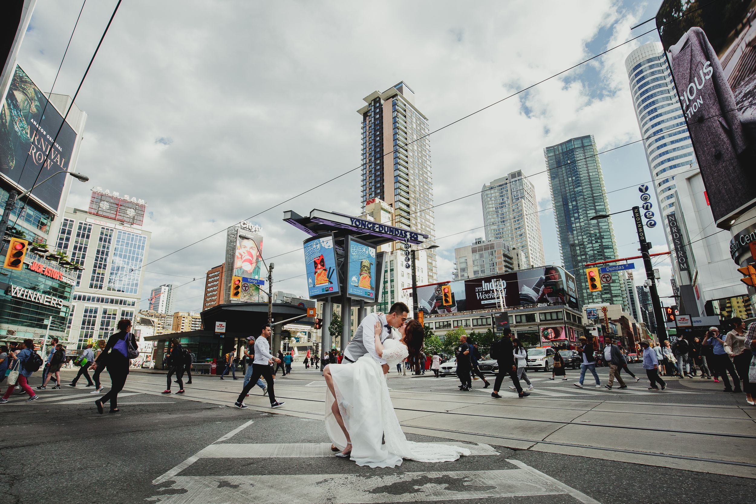 Wedding couple poses in busy downtown intersection surrounded by modern city buildings.