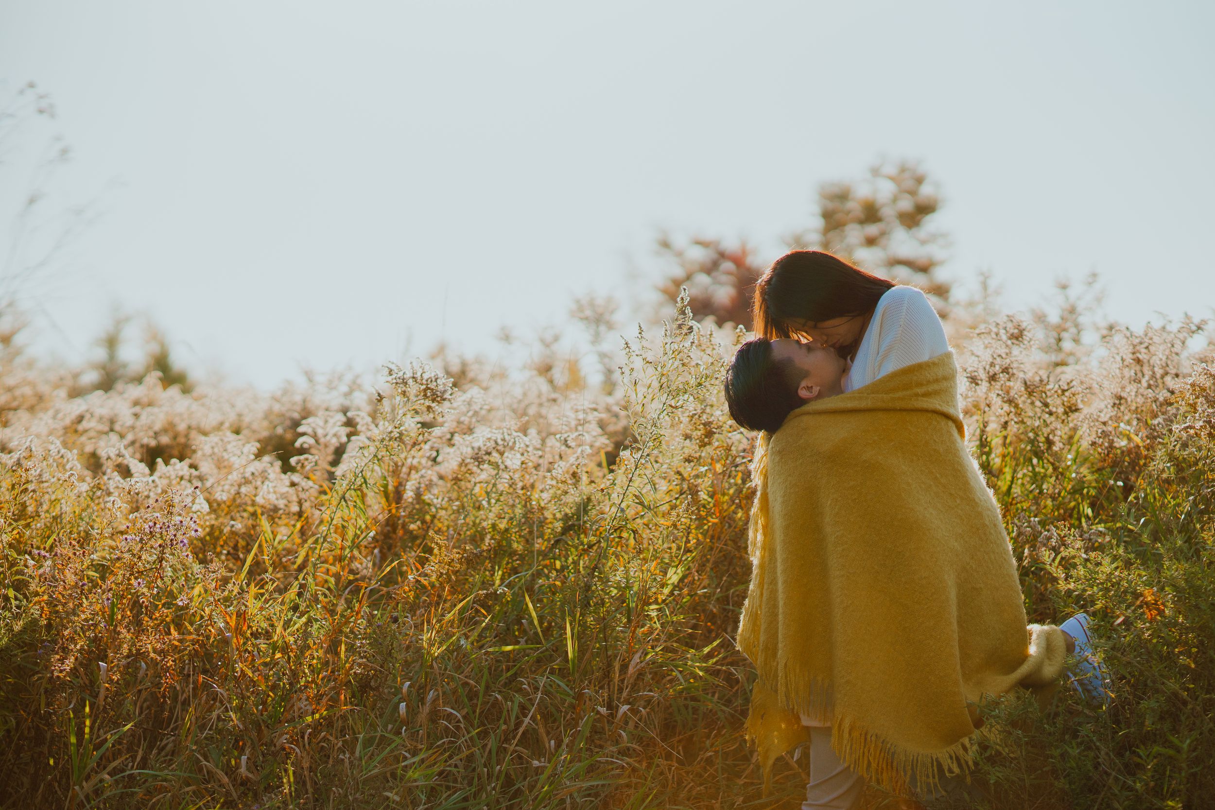 A tender moment wrapped in a yellow blanket during golden hour in a field.