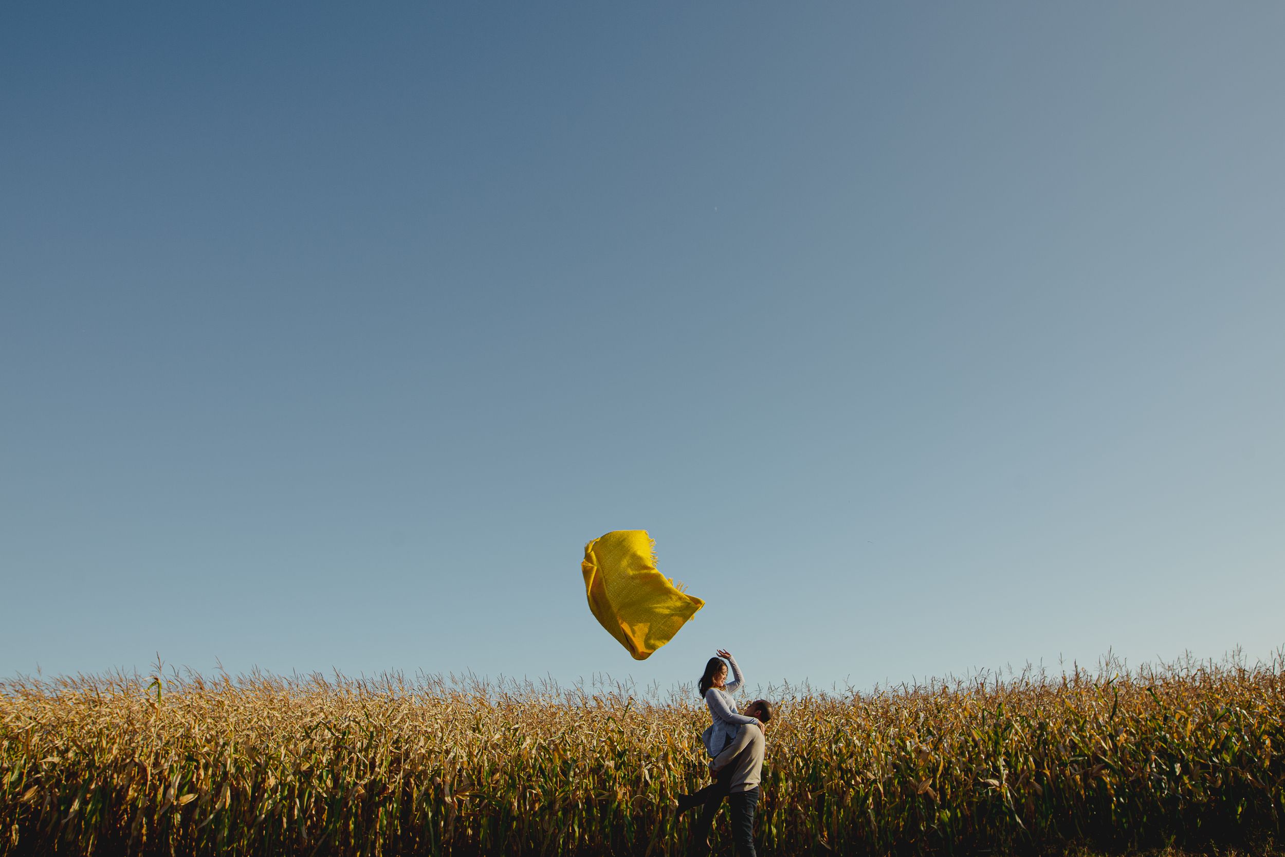 A yellow fabric billows in the air against a cornfield and blue sky.