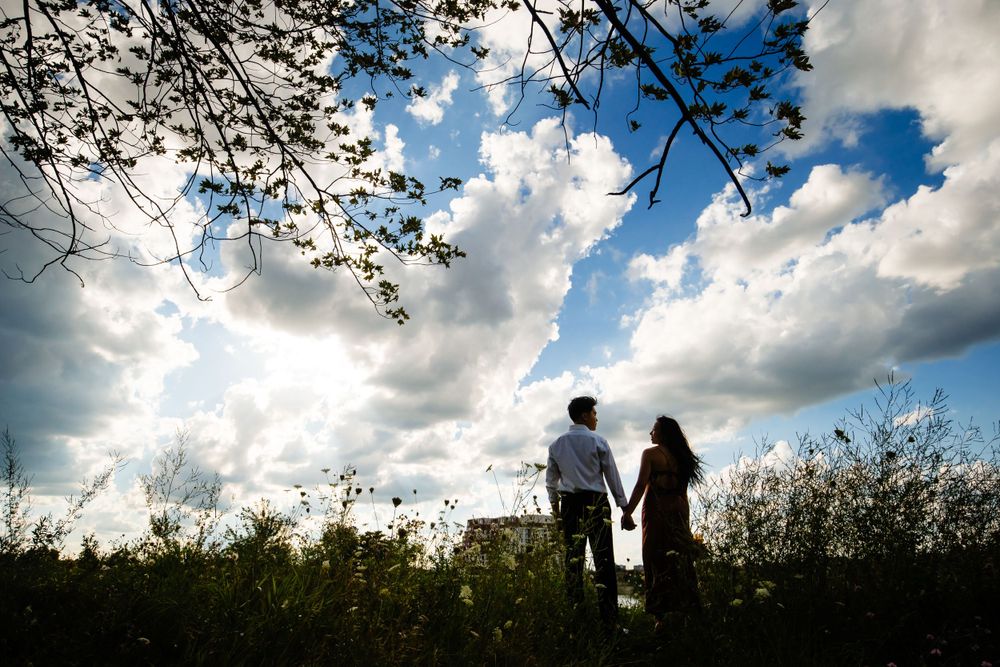 A couple stands hand in hand on a hilltop silhouetted against a dramatic sky with billowing clouds.