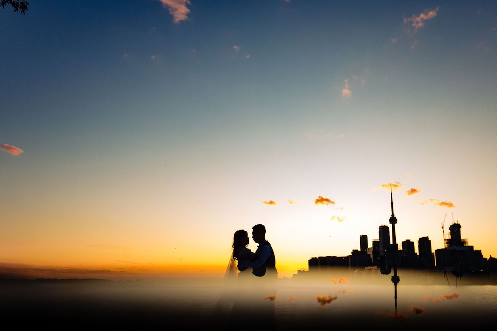 Silhouettes stand against a dramatic sunset skyline with a city backdrop in the distance.