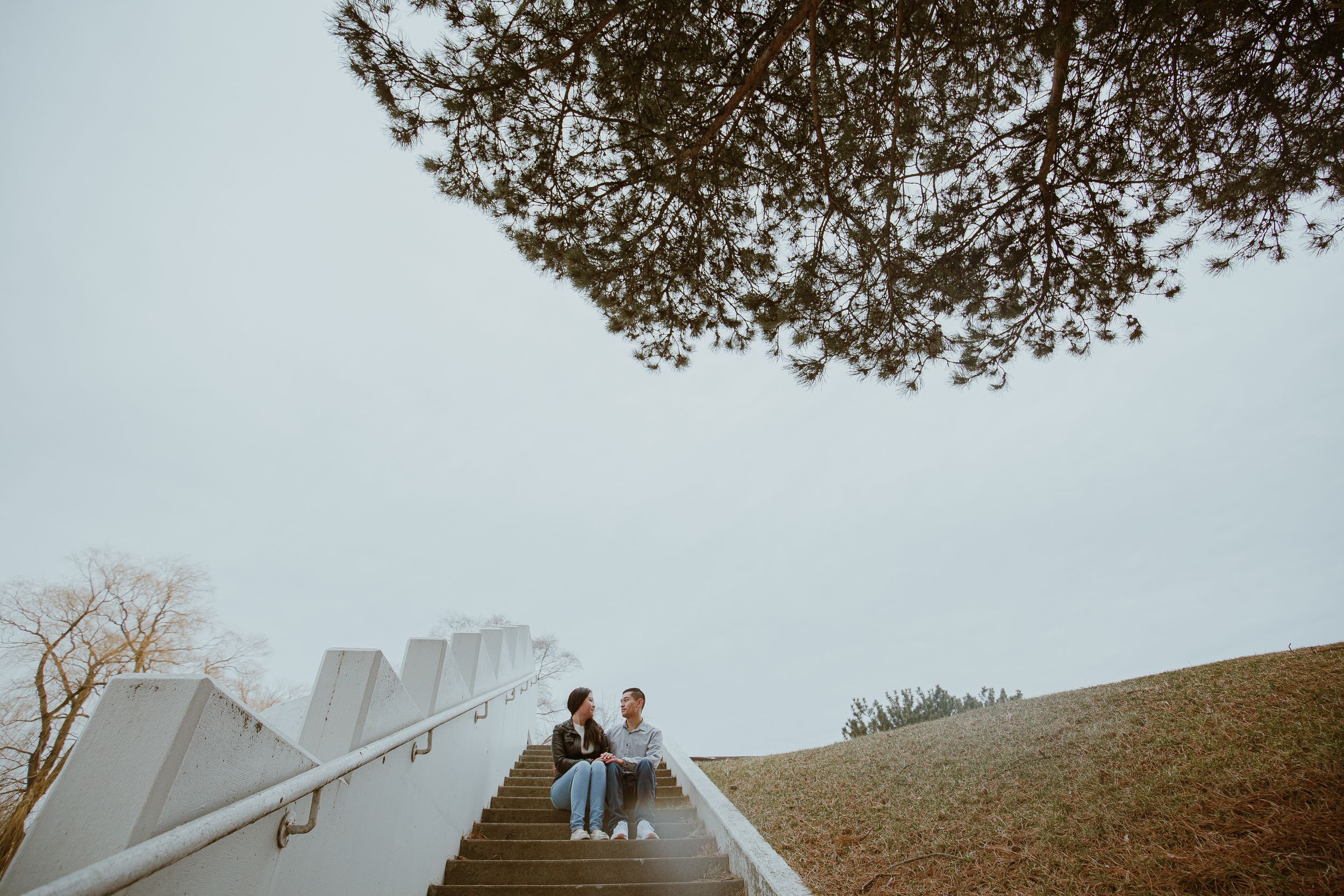 A couple stands on white concrete stairs against an overcast sky.