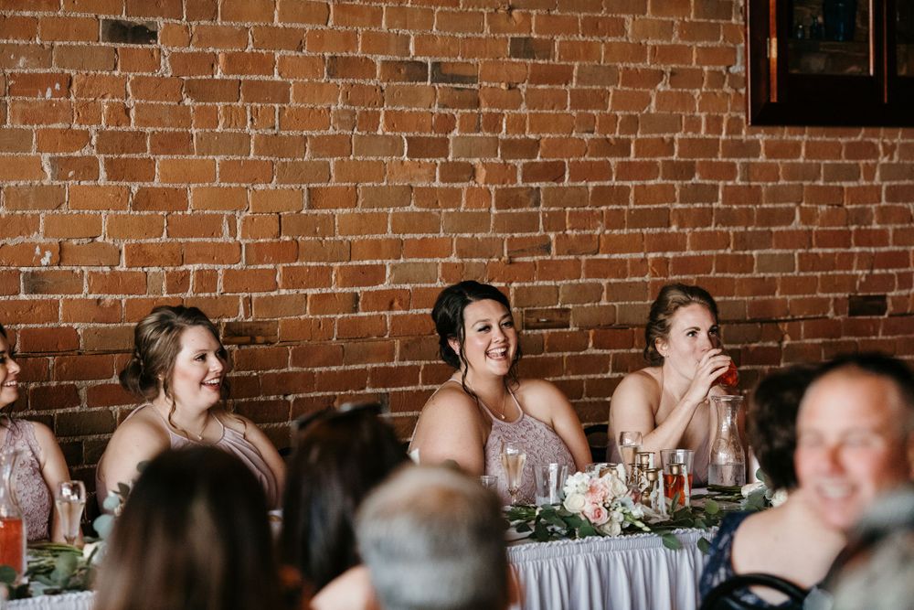 Bridesmaids in pink dresses laughing during wedding reception speeches.