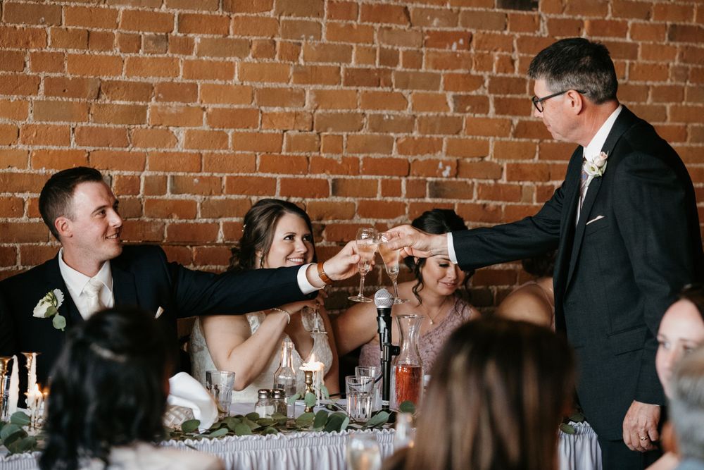Father of bride toasting with newlyweds at wedding reception dinner.