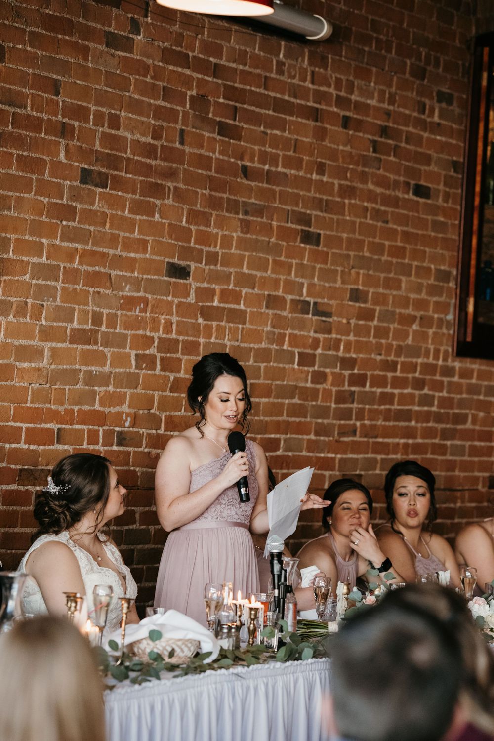 Bridesmaid in pink dress giving heartfelt speech at wedding reception.