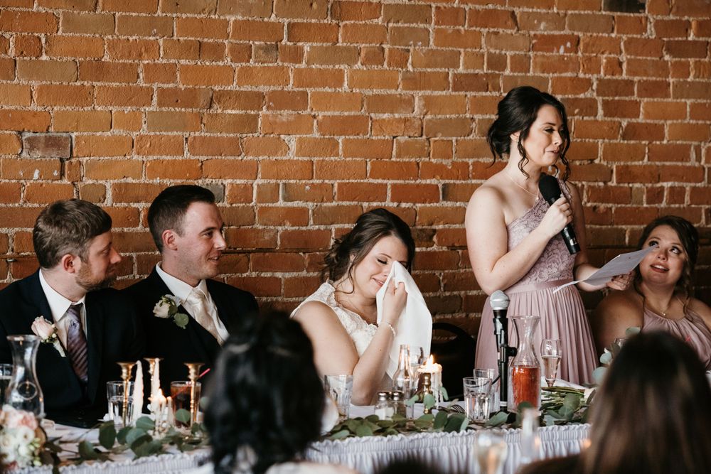 Emotional bride wiping tears during bridesmaid speech at wedding reception.