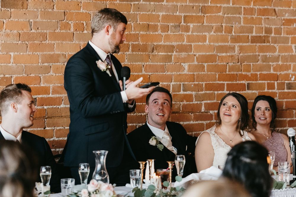 Best man giving toast to laughing bride and groom at reception.