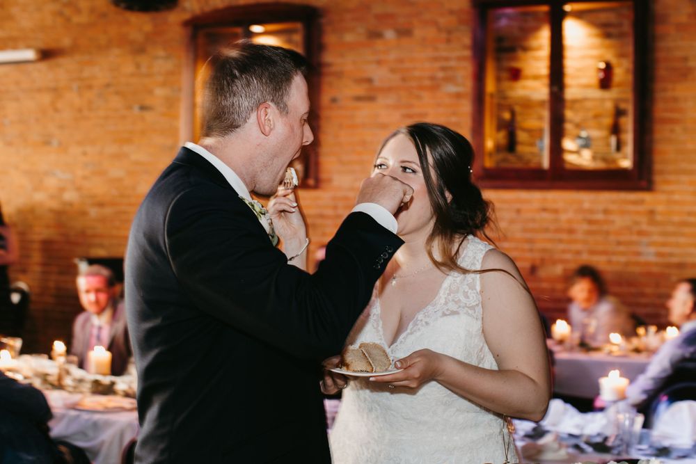 Groom feeding bride a piece of wedding cake during fun cake cutting ceremony at reception.