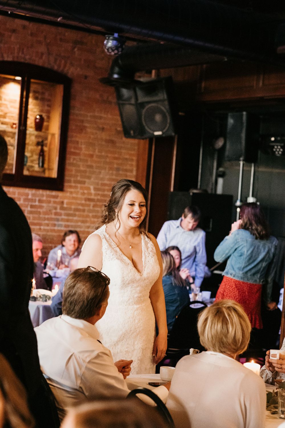 Radiant bride in lace gown smiling while mingling with guests at wedding reception.