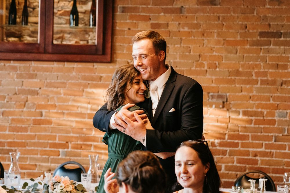 Older couple sharing a warm embrace at wedding reception near exposed brick wall.