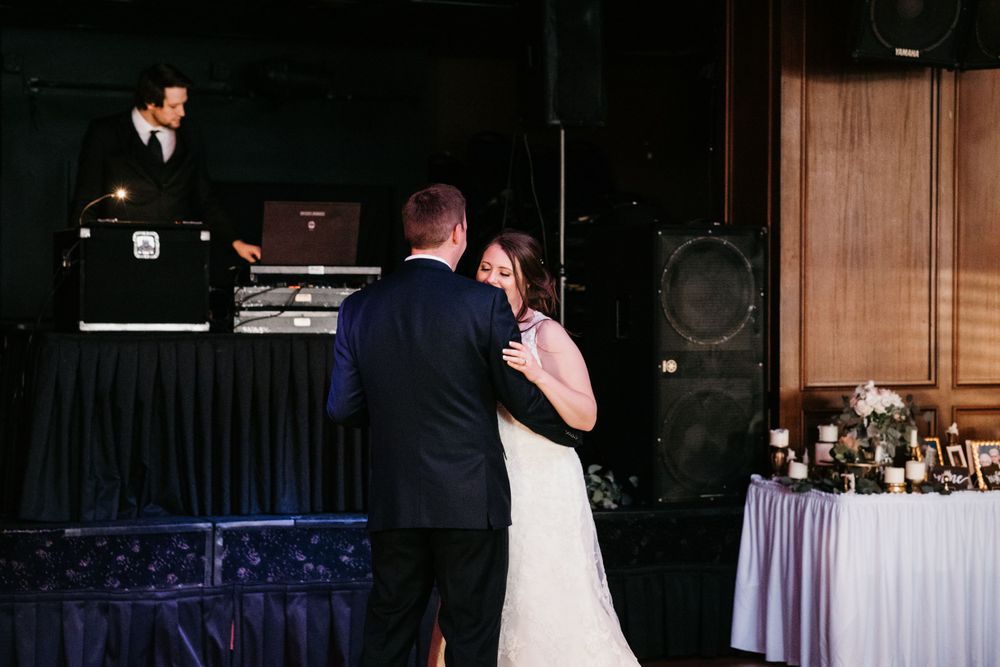 Newlyweds share intimate first dance while DJ performs on stage at elegant wedding reception.