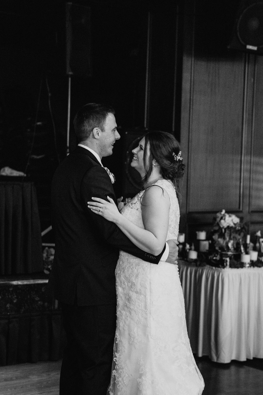 Black and white photo of smiling bride and groom sharing first dance at wedding reception.
