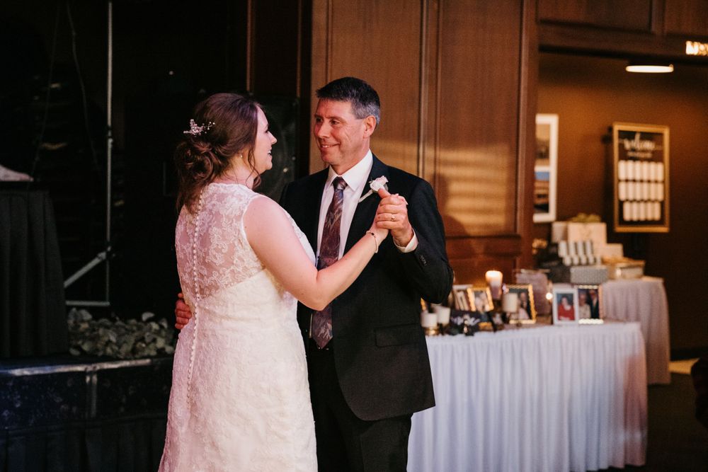 Bride shares a joyful father-daughter dance at wedding reception with gift table behind them.