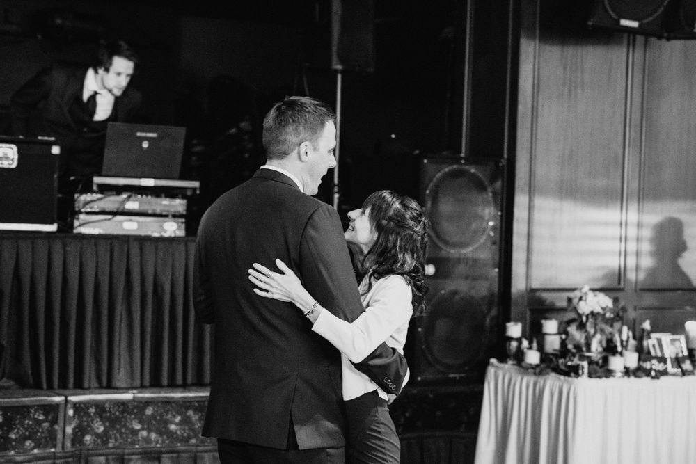 Black and white photo of couple sharing romantic dance at wedding reception with DJ in background.