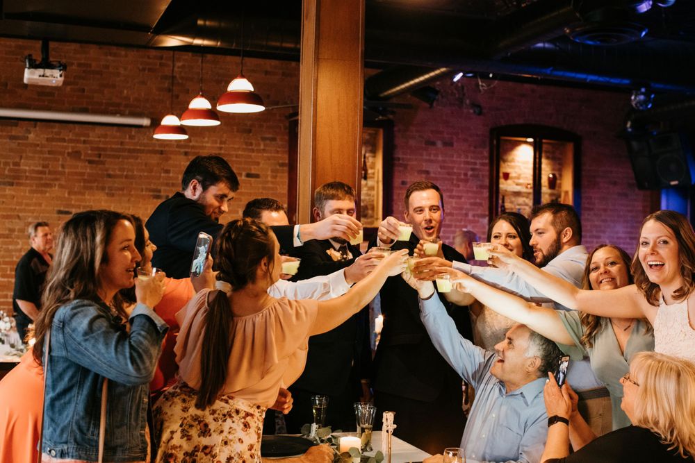 Wedding guests raise glasses in a celebratory toast at lively reception venue with brick walls.