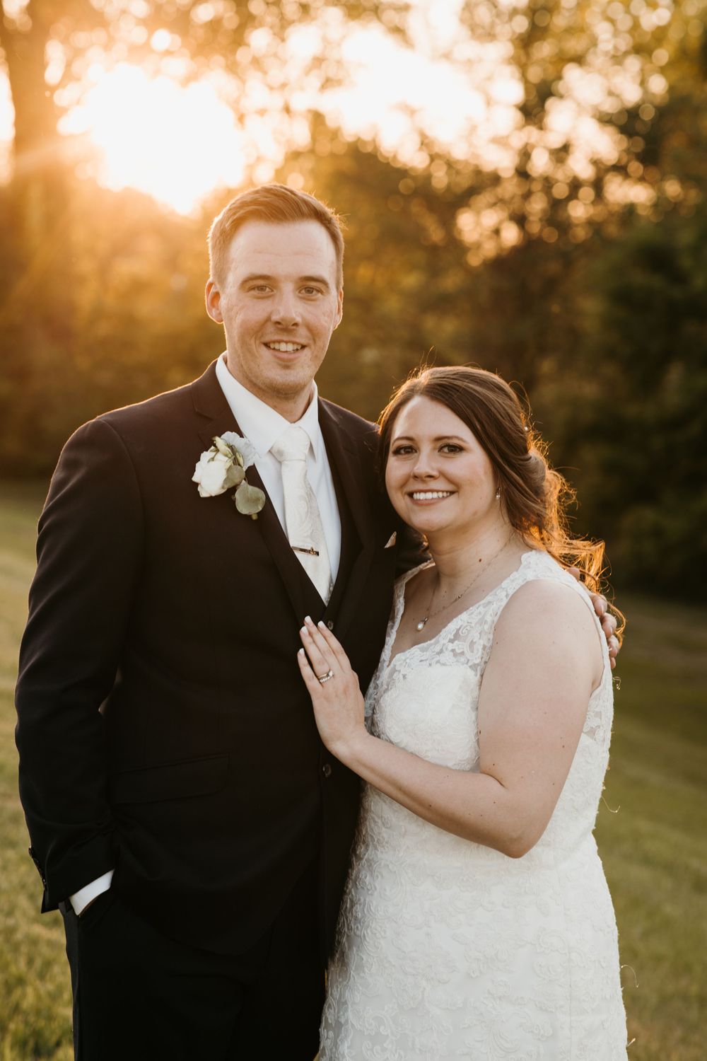 Bride and groom smiling at camera during golden hour sunset outdoor wedding portrait.